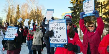 Members holding up signs that read "Alaska Nurses Association: Safe Staffing = Healthy Communities", "Help Us Help You", "Don't Cut Bedside Nursing" and more