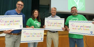 CFT members hold signs saying "All are welcome and safe here." and "Todos son bienvenidos y aquí están seguros."