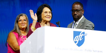 On the podium, Dolores Huerta waves to convention attendees, flanked by AFT officers Evelyn DeJesus and Fedrick Ingram.