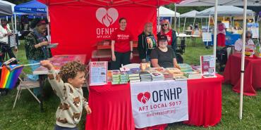 Young child with a Pride flag running in front of OFNHP booth at an outdoor event