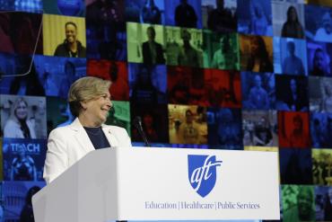 La presidenta de la AFT, Randi Weingarten, de pie detrás del podio, sonriendo mientras pronuncia su discurso.