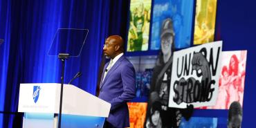 The Rev. Raphael Warnock, U.S. Senator from Georgia, stands at a podium in front of a images of AFT members and a sign that says "Union Strong"