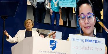 AFT President Randi Weingarten gestures while delivering the State of the Union speech from behind the podium at the AFT's national convention. She is wearing a white suit and standing in front of a backdrop of photos of union members.&nbsp;