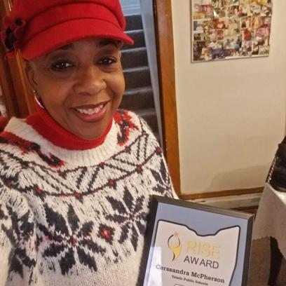 a black woman, Cerssandra McPherson, holds her award and smiles