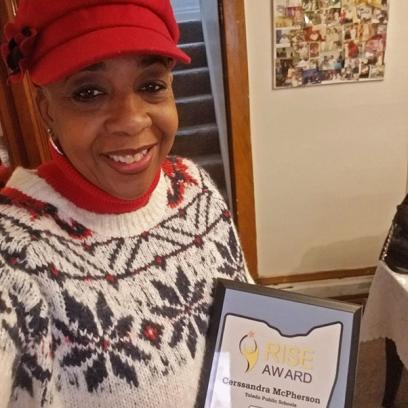 una mujer negra, Cerssandra McPherson, sostiene su premio y sonríe