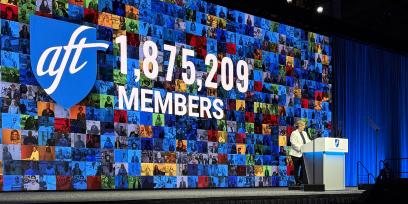 AFT President Randi Weingarten delivers the State of the Union speech from behind the podium at the AFT's national convention. She is wearing a white suit and standing in front of screen with the AFT's most recent membership number: 1,875,209.